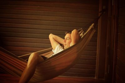 Young man relaxing on hammock against wooden wall