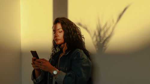 Young woman looking at camera while standing on mobile phone