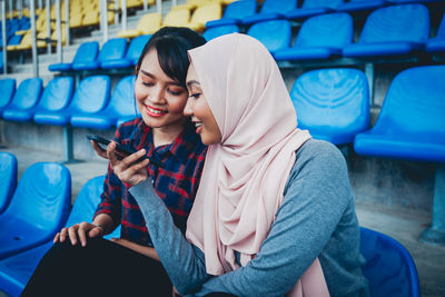 Young woman using mobile phone while sitting on laptop