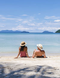 Rear view of woman sitting at beach against sky