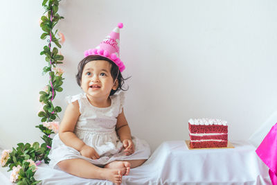 Portrait of cute girl sitting against wall