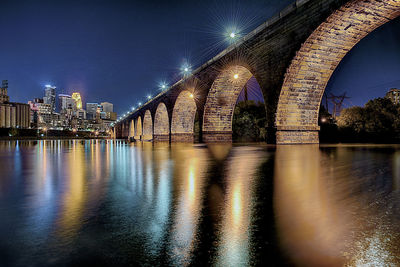 Illuminated bridge over river in city at night