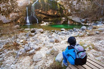 Rear view of men sitting on rock by river