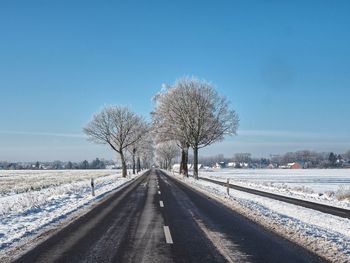 Snow covered road by trees against blue sky