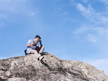 Low angle view of man sitting on rock against sky