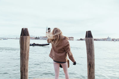 Rear view of young woman standing on jetty by canal against sky