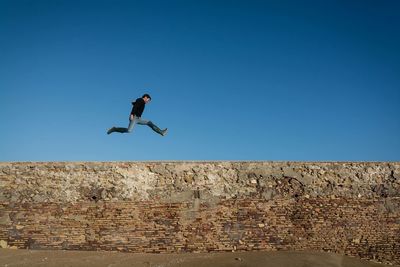 Low angle view of man jumping against clear blue sky