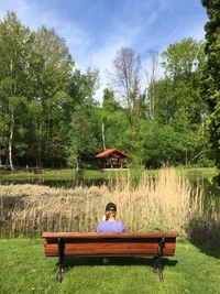 Man sitting on bench by lake against trees