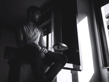 Side view of young man looking through window at home