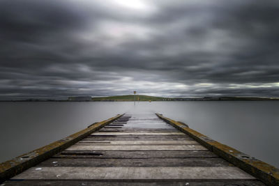 Wooden pier over sea against cloudy sky