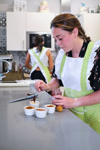 Women in aprons standing and preparing tasty desserts in light kitchen in cafeteria in daytime