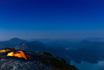 Illuminated tents on mountains against clear blue sky