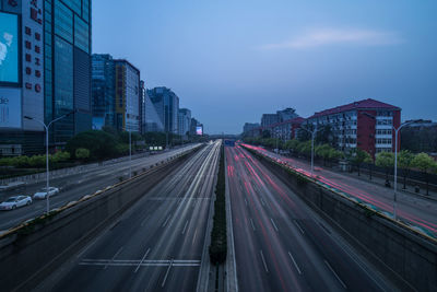 Light trails on road amidst buildings in city against sky