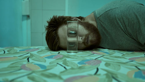 Portrait of young man lying by drinking glass on bed