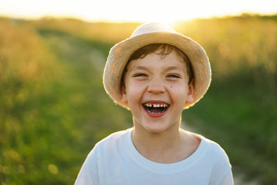 Portrait of a smiling little boy in a white t-shirt and hat playing outdoors on the field at sunset