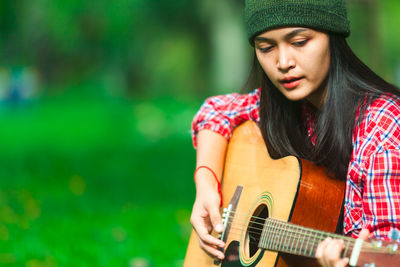 Young woman playing guitar while sitting at park