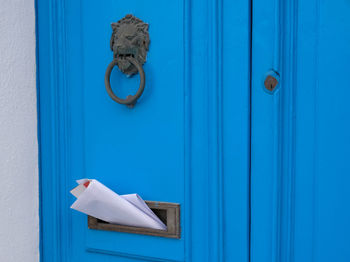 Blue vintage door with knocker in shape of lion, mailbox slot in door with advertising newspapers.