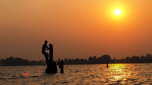 Silhouette people by lake against sky during sunset