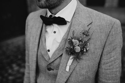 Close-up of man in a suit standing against blurred background with flowers