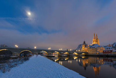 River in illuminated city against sky during winter