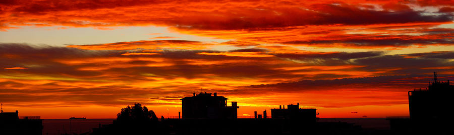 Silhouette of buildings against dramatic sky during sunset