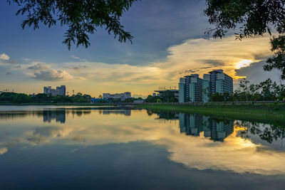 Scenic view of lake by buildings against sky during sunset