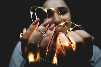 Close-up portrait of woman holding hands against black background