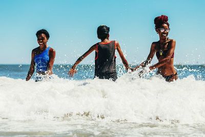 Friends playing in sea against clear blue sky on sunny day