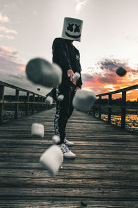 Man and woman standing by railing against sky during sunset