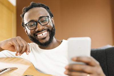 Smiling man using phone while sitting in studio