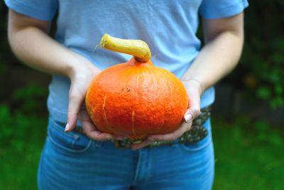 Midsection of man holding pumpkin while standing on field