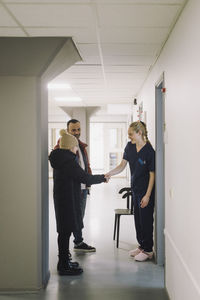 Female nurse shaking hand with girl standing by father at hospital