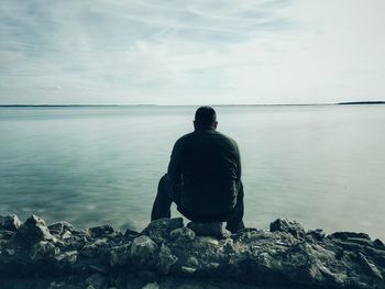 Rear view of man sitting at beach against sky