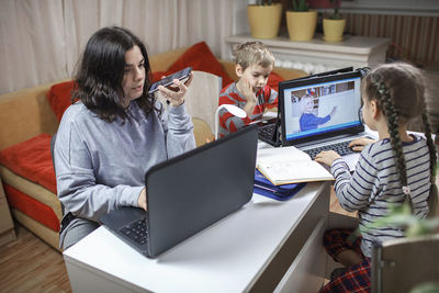High angle view of mother talking over phone by siblings studying over laptop at home