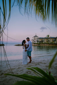 Couple standing at beach against sky during sunset