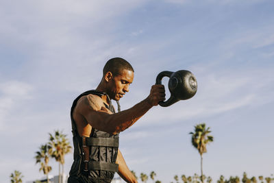 Mature sportsman practicing exercise with kettlebell under sky