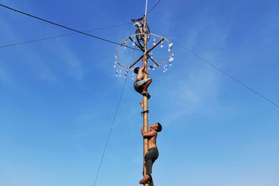 Low angle view of man climbing rope against blue sky