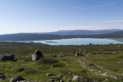 Rocks on grassy field by lake against blue sky