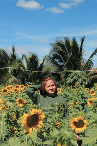Portrait of smiling young woman by sunflower on field against sky