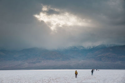 People on snowcapped mountain by sea against sky