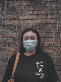 Portrait of young woman wearing mask standing against wall outdoors