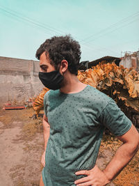 Young man looking away while standing against sky