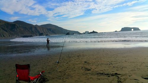 Man fishing while standing at shore of beach