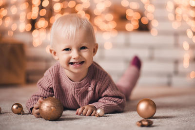 Happy child girl 1-2 year old wearing knitted sweater crawling on floor with christmas balls