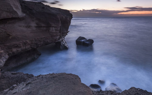 Rocks in sea against sky during sunset