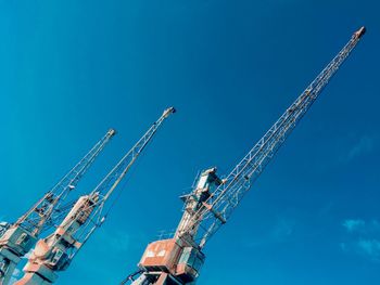 Low angle view of cranes against blue sky