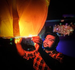 Young man holding paper lantern at night