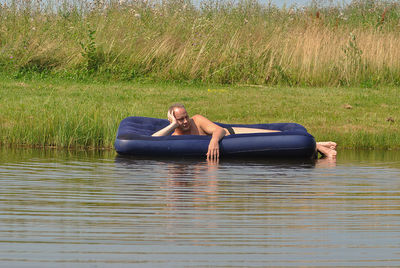 Shirtless man resting on pool raft in lake during sunny day