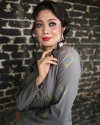 Portrait of young woman standing against brick wall