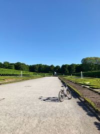 Bicycle parked on field by road against clear blue sky